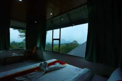 a person laying on a bed in a bedroom with a large window at Wayanad Cave N Pillar Resort in Sultan Bathery