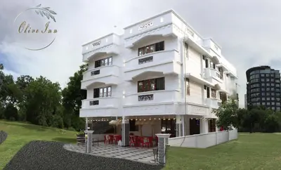 a white building with red tables in front of it at Olive Inn Apartment in Alwaye