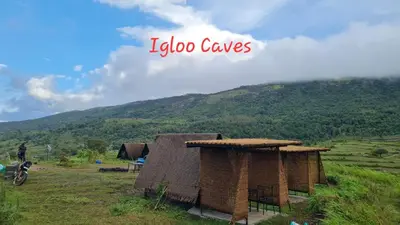 two thatched huts in a field with a mountain at Shining Caves Resort in Varagampadi