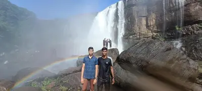 two men standing in front of a waterfall with a rainbow at Jewel Homes Thattekad - ISO 9001 certified Birding & Family Nature Stay in Thattakād
