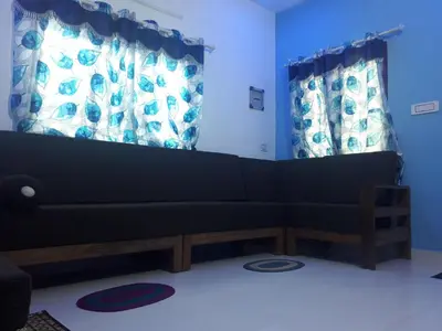 a living room with a black couch and two windows at Munnar Brindavan Cottage in Munnar