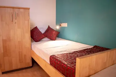 a small bed with red pillows next to a wooden cabinet at Roambay in Mysore
