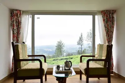 a living room with two chairs and a large window at Villa Sullivan by VEO - Part of StayVista in Ooty