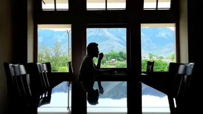a person sitting at a table looking out of a window at KTDC Garden House in Palakkad