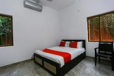 a bedroom with a bed and a chair and two windows at Hotel O Al Ameen Residency in Kannur