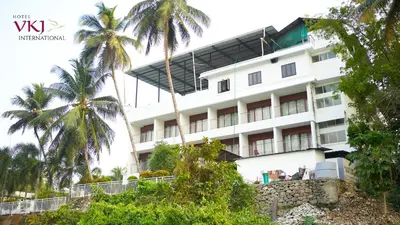 a hotel with palm trees in front of it at Hotel VKJ International Kuttampuzha in Thattakād