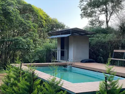 a swimming pool in a garden with a house at 900 Woods Wayanad Eco Resort - A Sprawling Jungle Stay near Glass Bridge in Meppādi