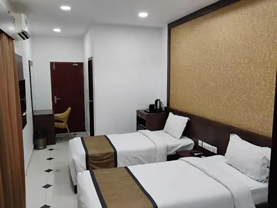 a hotel room with two beds and a chair at Hotel Emperor in Kannur