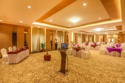 a banquet hall with white tables and chairs and a person at Emerald Clarks Inn Suites in Mysore