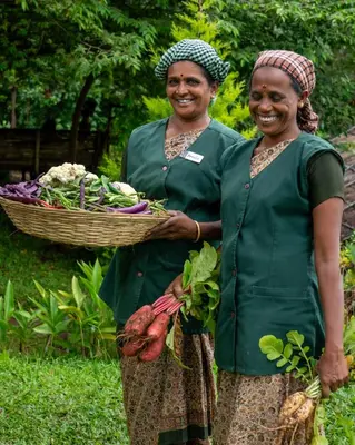 two women standing next to each other holding a basket of vegetables at The Mudhouse Marayoor in Munnar