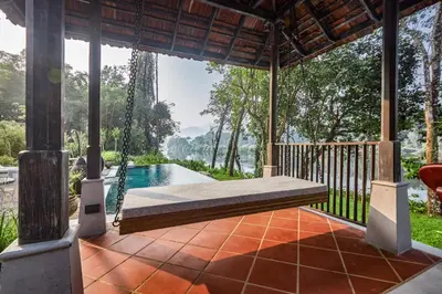 a porch with a swing and a swimming pool at Periyar River Lodge in Thattakād