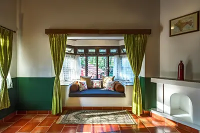 a room with a couch in front of a window at SaffronStays Calamondinn Bungalow - 5BR Colonial Heritage Home within Coffee Plantation in Coorg in Gonikoppal