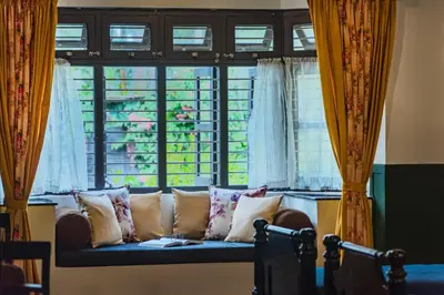 a couch sitting in front of a window at SaffronStays Calamondinn Bungalow - 5BR Colonial Heritage Home within Coffee Plantation in Coorg in Gonikoppal