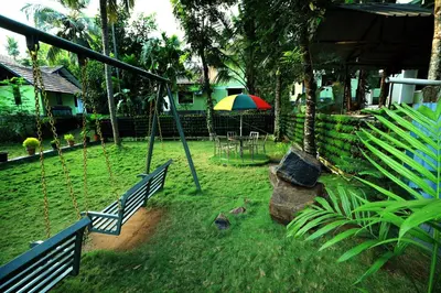 a swing in a yard with a table and umbrella at NARMADA HOMESTAY Ganga in Perintalmanna