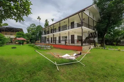 a woman laying in a hammock in front of a house at Lhasa Ayurveda and Wellness Resort - A BluSalzz Collection, Kochi, Kerala in Cochin