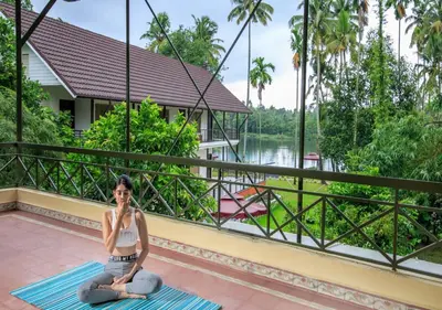 a woman sitting on a mat on a balcony with a view of a river at Lhasa Ayurveda and Wellness Resort - A BluSalzz Collection, Kochi, Kerala in Cochin