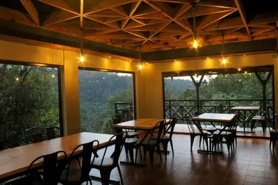 a dining room with tables and chairs and windows at The Wild Trails Clarks Exotica , Munnar in Munnar
