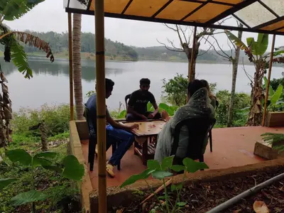 a group of people sitting around a table near a lake at 7 Heaven Resorts in Ambalavayal