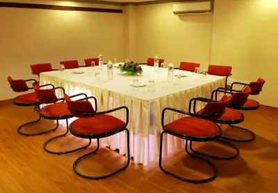 a conference room with a white table and red chairs at Manuelsons Malabar Palace in Kozhikode
