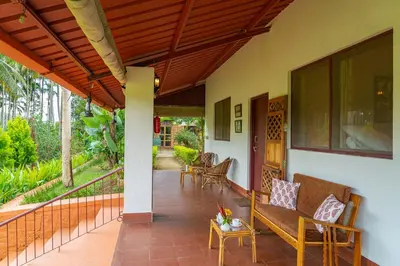 a porch of a house with a bench and a table at 5BR Firefly By The River with Breakfast - Nature's Lap in Kushālnagar