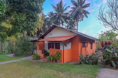 a red and white house with palm trees in the background at 5BR Firefly By The River with Breakfast - Nature's Lap in Kushālnagar