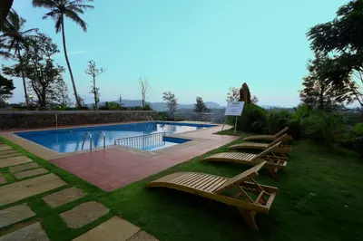 a swimming pool with three lounges and a row of chairs at Parisons Plantation Experiences by Abad in Mananthavady