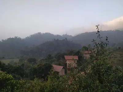 a group of houses on a hill with mountains in the background at BARSATI Ranches in Vythiri