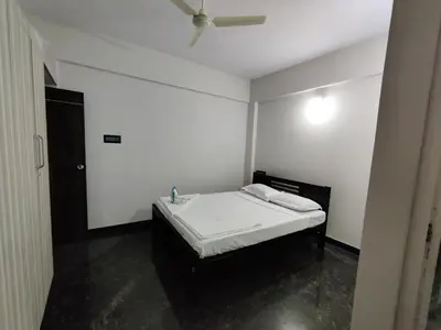 a white room with a bed and a ceiling fan at Royal Wings Apartments in Mysore