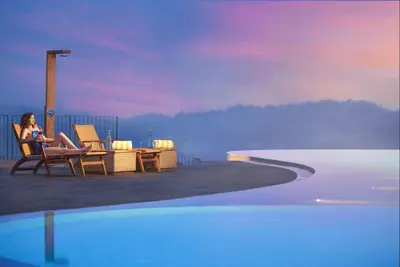 a woman sitting in a chair next to a swimming pool at MOUNTAIN SHADOWS RESORT Wayanad in Wayanad