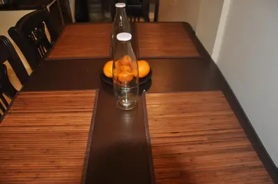 a table with a bottle and a bowl of oranges on it at Little House Ooty in Ooty
