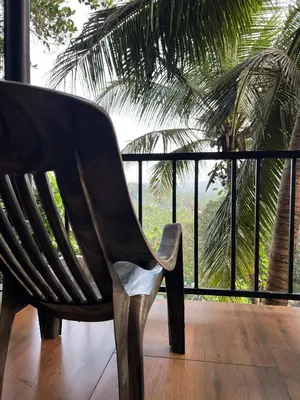 a wooden chair sitting on a porch with a palm tree at Casita Greens in Kondotti
