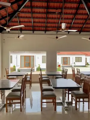 a dining room with tables and chairs and windows at MALLI resort in Dhārāpuram