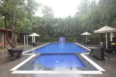 a swimming pool with chairs and umbrellas in a yard at Regenta Jungle Resort Kabini Springs in Begūr