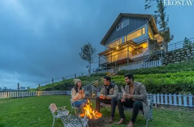 three people sitting around a fire in front of a house at EKO STAY - Woodside Ivy in Ooty