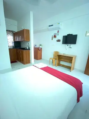 a bedroom with a white bed and a kitchen at DOLPHIN ENCLAVE SERVICE STUDIO APARTMENTS in Kalpetta