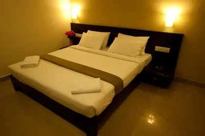 a bedroom with a large bed with white sheets and pillows at Hotel Sunshine in Mysore