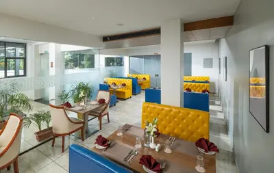 a restaurant with yellow booths and tables and chairs at Oshin Wayanad in Wayanad
