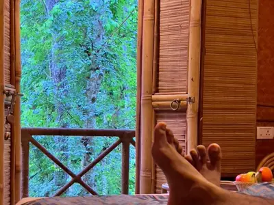 a person with their feet up on a bed looking out a window at Adrak Mountain Mist Forest Resort in Pulpally