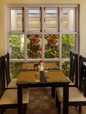 a table with chairs and a window with flowers at Rosewood by Nature Resorts and Stays in Ooty