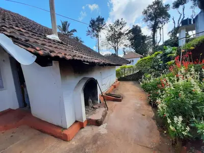 a small white house with a yard with flowers at Sardar Bahadur's Heritage Bungalow Estate Stay in Napoklu