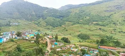 a village on a hill with mountains in the background at Misty Mountains Holiday Homes in Vattavada