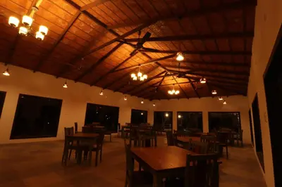 a dining room with wooden tables and chairs and lights at Havon Plantation Resorts in Varagampadi