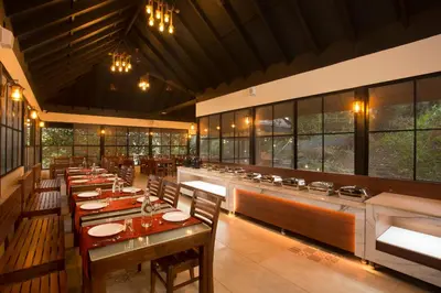 a restaurant with wooden tables and chairs and windows at Amrezy Resort and Spa by Stride, Wayanad in Vythiri