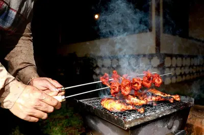 a person cooking meat on a grill with tongs at SaffronStays Coorg Toddy Farms, Coorg in Madikeri