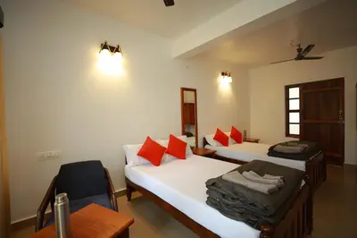 a room with two beds and a chair and a table at Ayla Homes in Madikeri