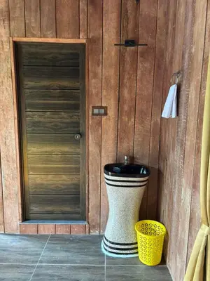 a bathroom with a toilet next to a wooden wall at Cure Monastery Family Resort in Marayoor