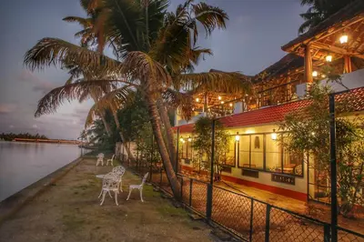 a building with chairs and a palm tree next to the water at Vala House - Full Villa in Pallipuram
