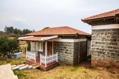 a brick house with a porch and a white fence at Tranqville Resorts in Ooty