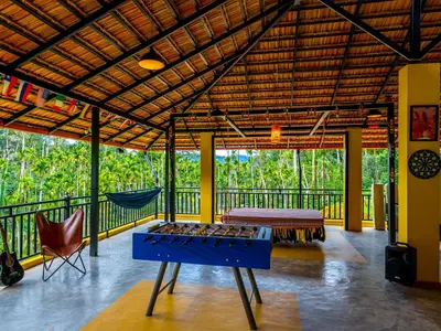 a room with a table and a hammock on a balcony at The Hosteller Coorg Rainforest, Madikeri in Madikeri