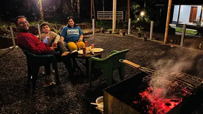 a group of three people sitting around a grill at Cave Valley Wayanad in Ambalavayal